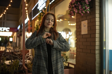 Portrait of a young beautiful cheerful red-haired girl in an evening autumn city.