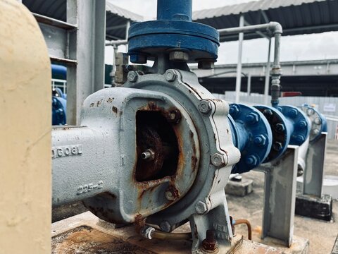 Close-up of an old industrial pump with cracked paint and visible rust, showcasing aging equipment in a heavy-duty mechanical system.