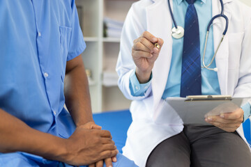 Doctor holding medical form having discussion with patient in hospital room. Patient and a surgeon...