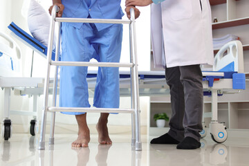 Doctor in a hospital is helping a male patient with weak leg muscles learn to walk with a cane. Physiotherapist doing physiotherapy for man practicing walking in the hospital room.