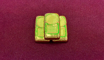Three gold bar are elegantly arranged on a deep red velvet cloth. Their shiny surface reflect light. The setting create a luxurious atmosphere.