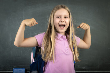 Schoolgirl showing her muscles in front of a chalkboard at school