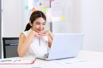 businesswoman sitting at the table while busy working on laptop computer at the office. Woman typing document, checking email, participating in online meeting at workplace.