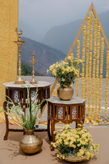 Elegant Indian wedding decor featuring brass lamps, vases of yellow chrysanthemums, wooden tables...