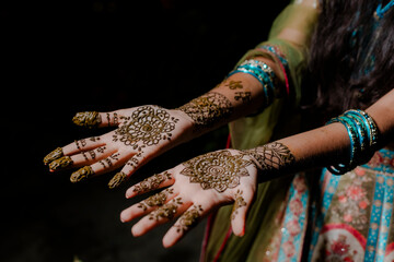 Elaborate henna designs adorn hands, wrists with bangles. Rich detail, cultural artistry shine.