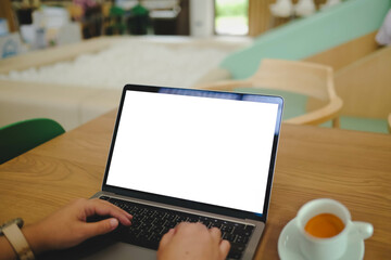 A person works on a laptop with a blank white screen in a kids' cafe or play area, illustrating remote work and family lifestyle.