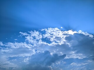 Sun's rays pierce through dramatic clouds in a vibrant blue sky, creating a beautiful and dynamic...