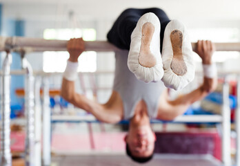 Gymnast performs complex tricks on horizontal bar in gym