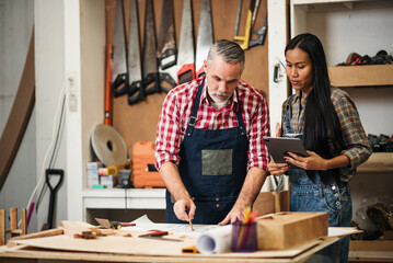 Senior Carpenter and Young Female Designer Collaborating on Furniture Design Sketch in Wood Workshop for Construction Project