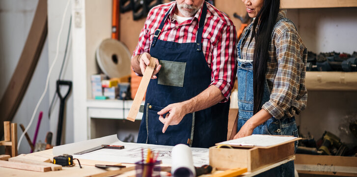 Senior Carpenter and Young Female Designer Collaborating on Furniture Design Sketch in Wood Workshop for Construction Project