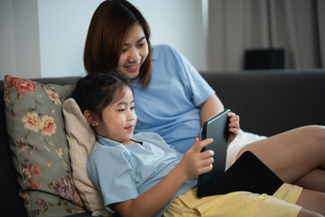 Enjoying Quality Time Together: Mother and Daughter Interacting with Tablet on Couch in Cozy Living Room Setting