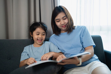 Joyful mother and daughter reading together on a couch in a cozy living room with natural light, sharing moments of laughter and learning