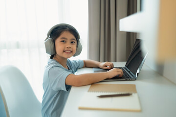 Young girl using laptop at home with headphones, smiling and engaging in online learning or gaming...