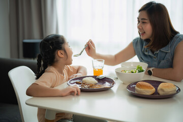 Joyful Moment at Home: A Mother Feeds Her Daughter Healthy Meal During Family Lunch Time in Modern Bright Dining Room Environment