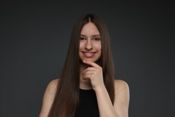 Portrait of smiling teenage girl with healthy long hair on dark grey background