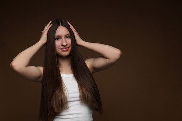 Portrait of beautiful teenage girl with healthy long hair on brown background. Space for text