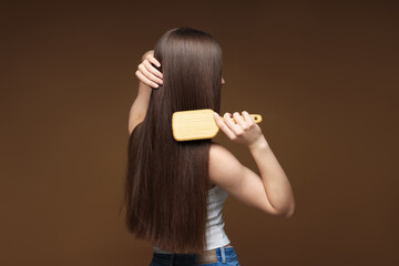 Teenage girl brushing her healthy long hair on brown background