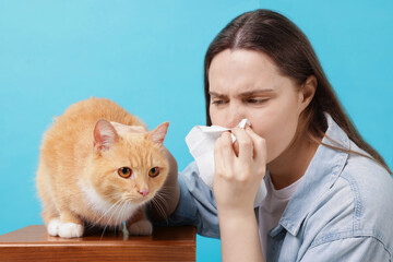 Woman suffering from allergy with her cat on light blue background