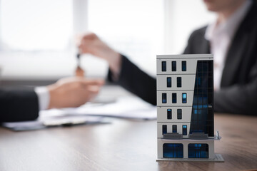 Real estate agent giving key to client at desk in office, focus on house model