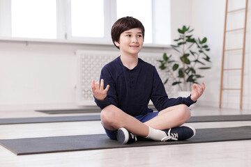 Happy boy practicing yoga on mat indoors