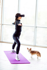 Charming woman practicing virtual reality yoga with dog in sunlit modern interior for fitness and...