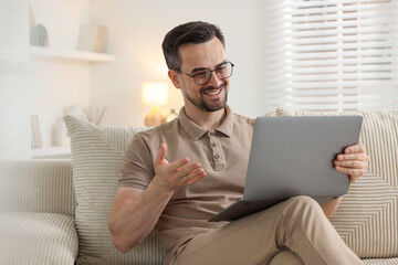 Professional psychologist having online consultation with his client via laptop on sofa indoors
