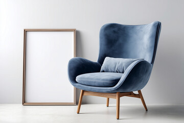 A stylish blue armchair with a high back and plush cushion stands beside a blank wooden-framed picture frame against a light wall, creating a modern and elegant atmosphere.