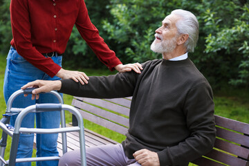 Caregiver supporting elderly man with walking frame outdoors, closeup