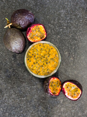 A bowl filled with passion fruit pulp, surrounded by whole and halved Passion Fruits
