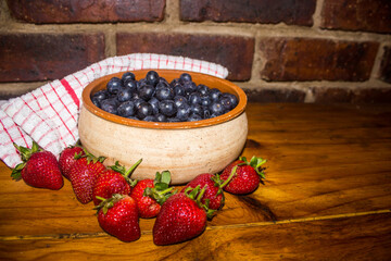 Rustic composition of a bowl of blueberries, surrounded by succulent red strawberries