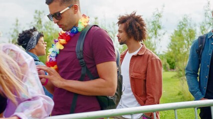 Camera tracks along group of young friends waiting behind barriers at entrance to music festival site checking mobile phones- shot in slow motion