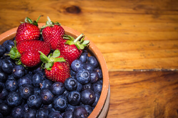 A rustic Bowl with a few bright red strawberries, on top of a large amount of indigo-colored...