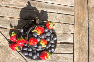 A lay-flat composition of a teacup filled to overflowing with strawberries and blueberries on a...