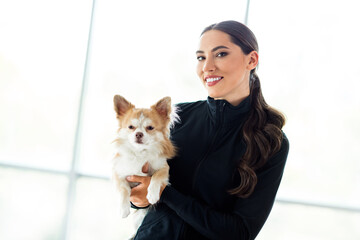 Charming Young female athlete holding a small dog during a gym break in a well-lit indoor studio