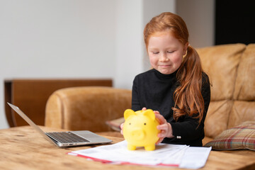 Young girl smiles while saving money in a piggy bank at home during the afternoon