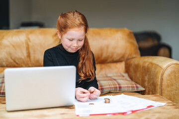 Young girl studying and counting coins at home on a cozy couch during a quiet afternoon
