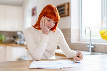 Woman reacts with concern while reviewing documents at home in a bright kitchen during daytime