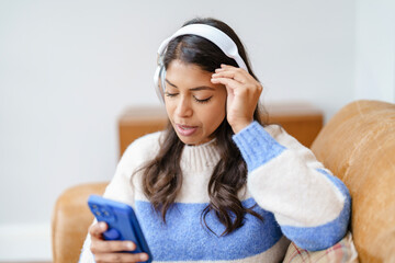 Woman listens to music on her smartphone while relaxing on a cozy couch in her stylish living room during the afternoon