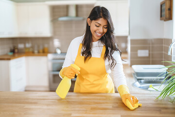 Woman wearing yellow gloves cleans kitchen countertops while smiling in a bright, modern home in...