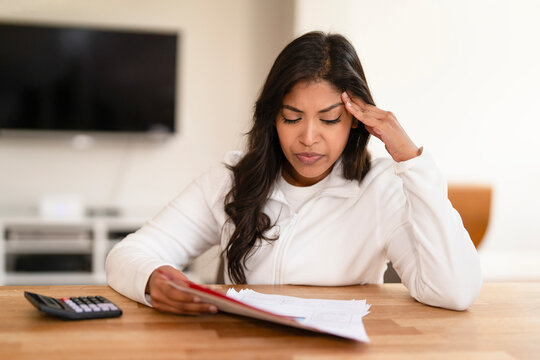 Young woman reviewing financial documents at home while looking concerned about her budget and expenses