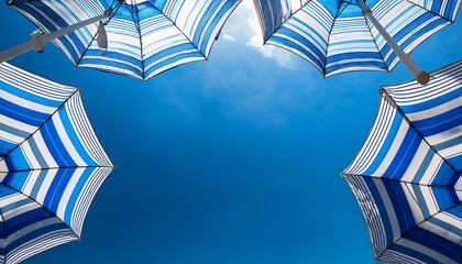 several summer bright white and blue striped beach umbrellas against a bright blue sky viewed from below summertime season banner with text space