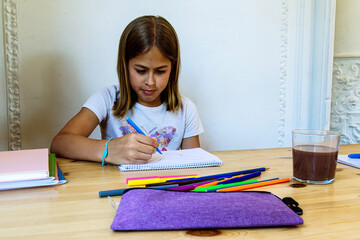 Young girl drawing on notebook with colored pencils and markers at home