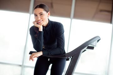 Young sportswoman smiling confidently during cardio workout indoors, embracing a fit and healthy...