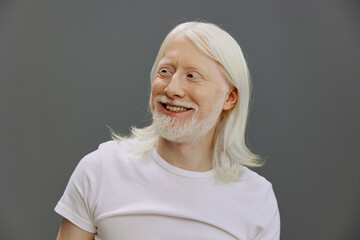 Portrait of a smiling elderly man with long white hair against a neutral gray background, conveying...