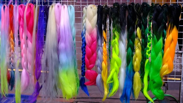 A row of colorful hair extensions are displayed on a rack. The colors include pink, blue, yellow, and green