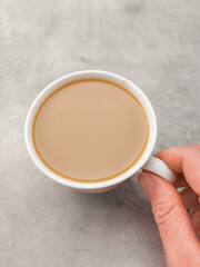 Hand holding cup of coffee with milk on marble table