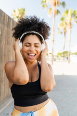 Curvy Hispanic sportswoman listening music with wireless headphones during fitness workout outdoors