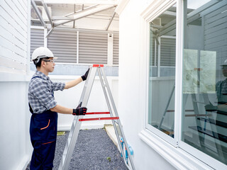 Asian male construction worker or housing project foreman adjusting an aluminium ladder under the...