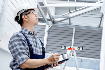 Professional building inspector man in protective workwear using digital tablet checking quality of...