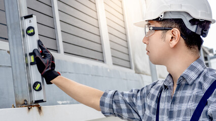 Asian male construction worker using level tool on fence. Home builder man checking the vertical plane of steel column. Measuring tool for building measurement and inspection